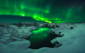 Las auroras boreales se reflejan sobre un río tranquilo en el Parque Nacional Thingvellir, parte del Círculo Dorado de Islandia, con nieve.