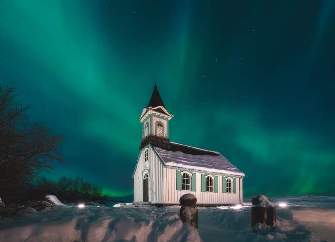 The northern lights dance above a snow-covered church in Iceland, creating a peaceful and magical winter scene.