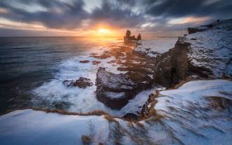 Coucher de soleil sur les falaises de Londrangar saupoudrées de neige sur la péninsule de Snaefellsnes, en Islande, avec les vagues s'écrasant sur les aiguilles rocheuses volcaniques.