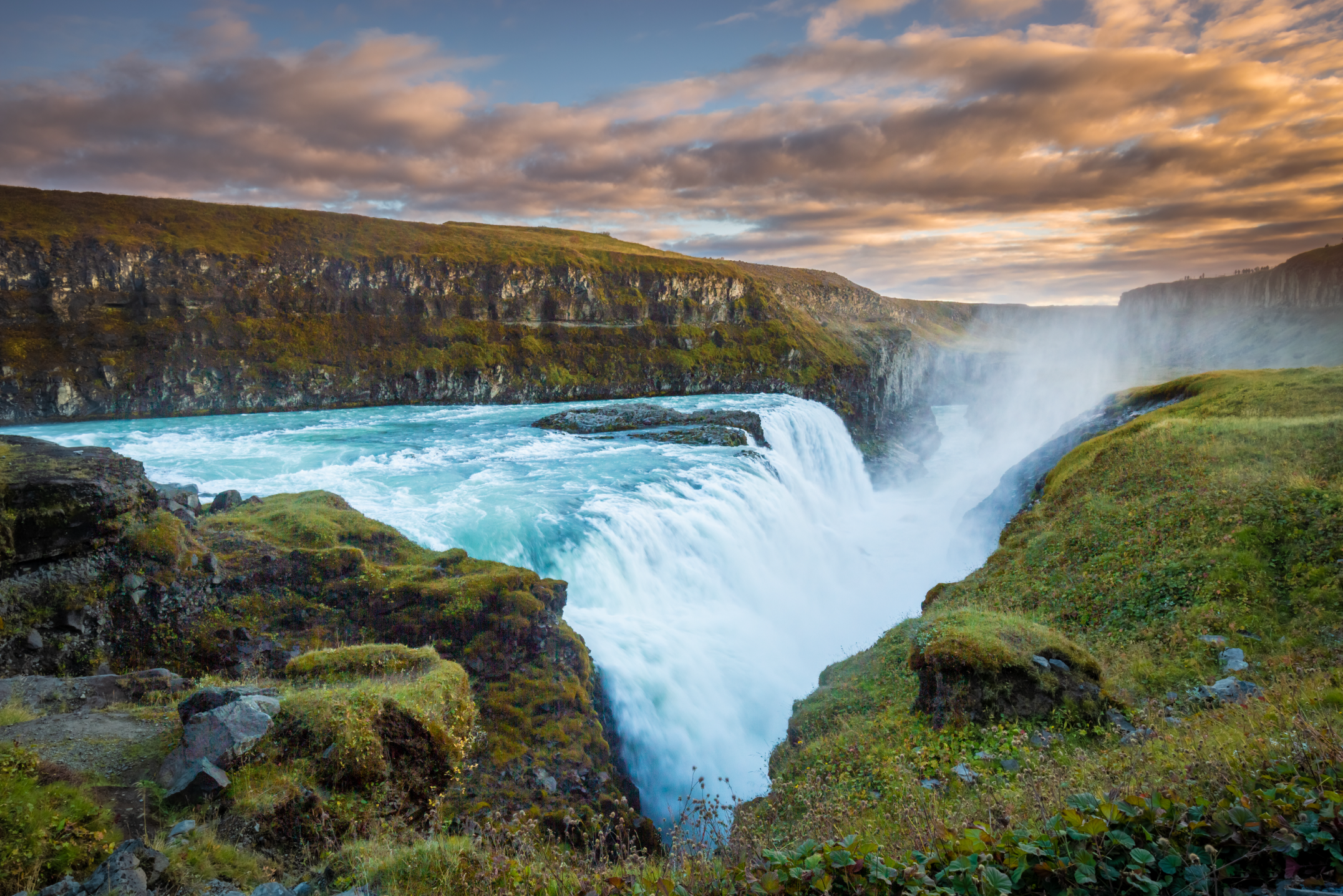 Cascata di Gullfoss al Circolo d'Oro, in Islanda, con le acque blu vibranti che scendono sulle rocce al tramonto.