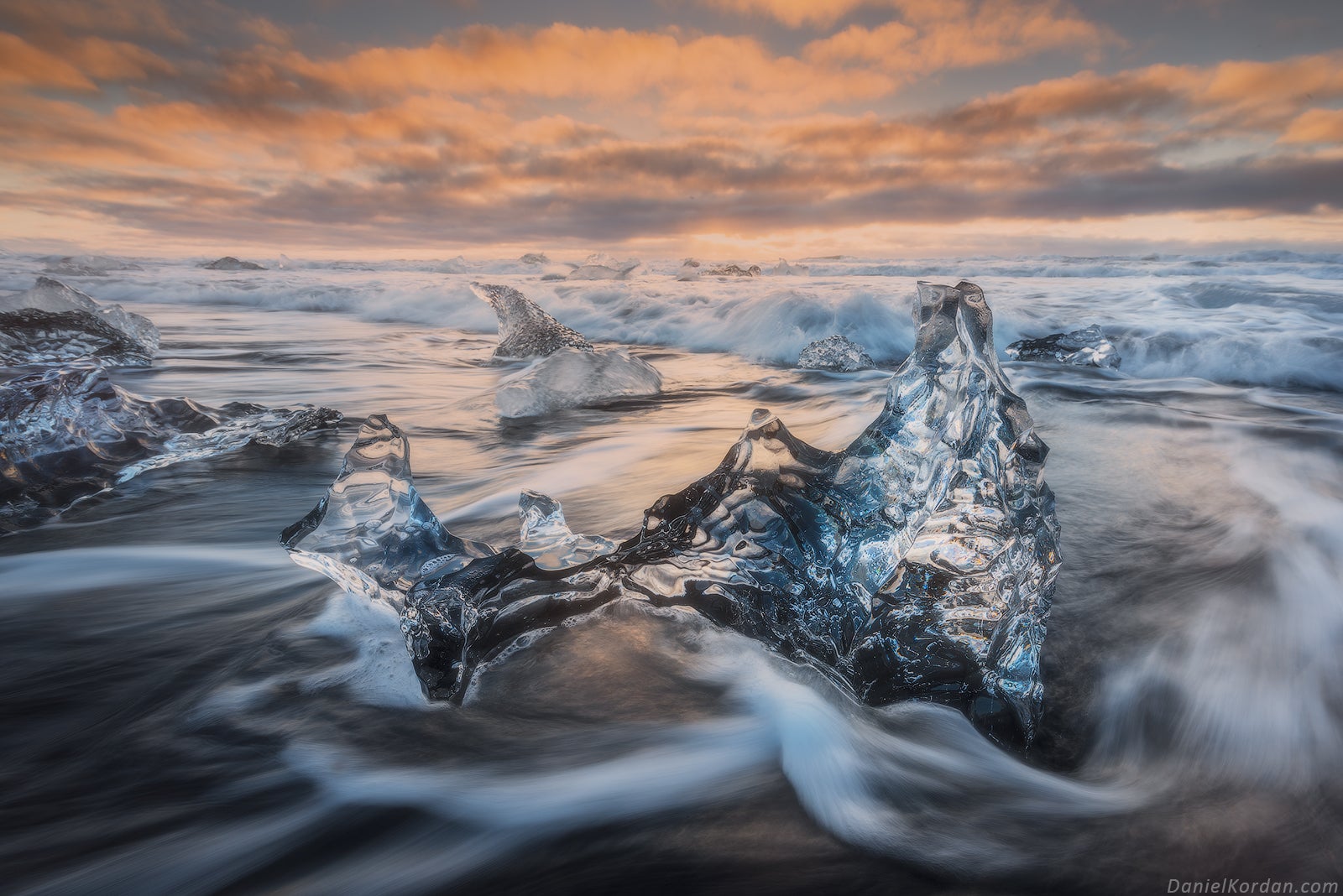 Des blocs de glace scintillent dans les vagues sur la Plage de diamants en Islande, illuminés par un lever de soleil coloré.