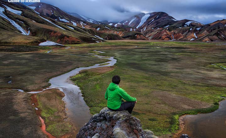 Человек сидит на краю горы с видом на Ландманналаугар в Исландии.