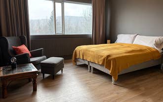 Interior of a Heima at Selfoss bedroom featuring a double bed with a yellow blanket, a gray armchair with an orange pillow, and