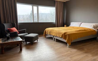 Chambre de Heima at Selfoss avec un lit double recouvert d’un plaid jaune, un fauteuil gris avec coussin orange.