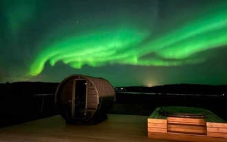 Northern lights illuminating the sky above the villa’s deck, with a hot tub and sauna in the foreground.