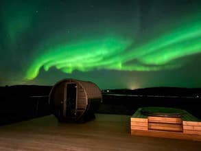 Nordlys, der oplyser himlen over villaens terrasse med udespa og sauna i forgrunden.