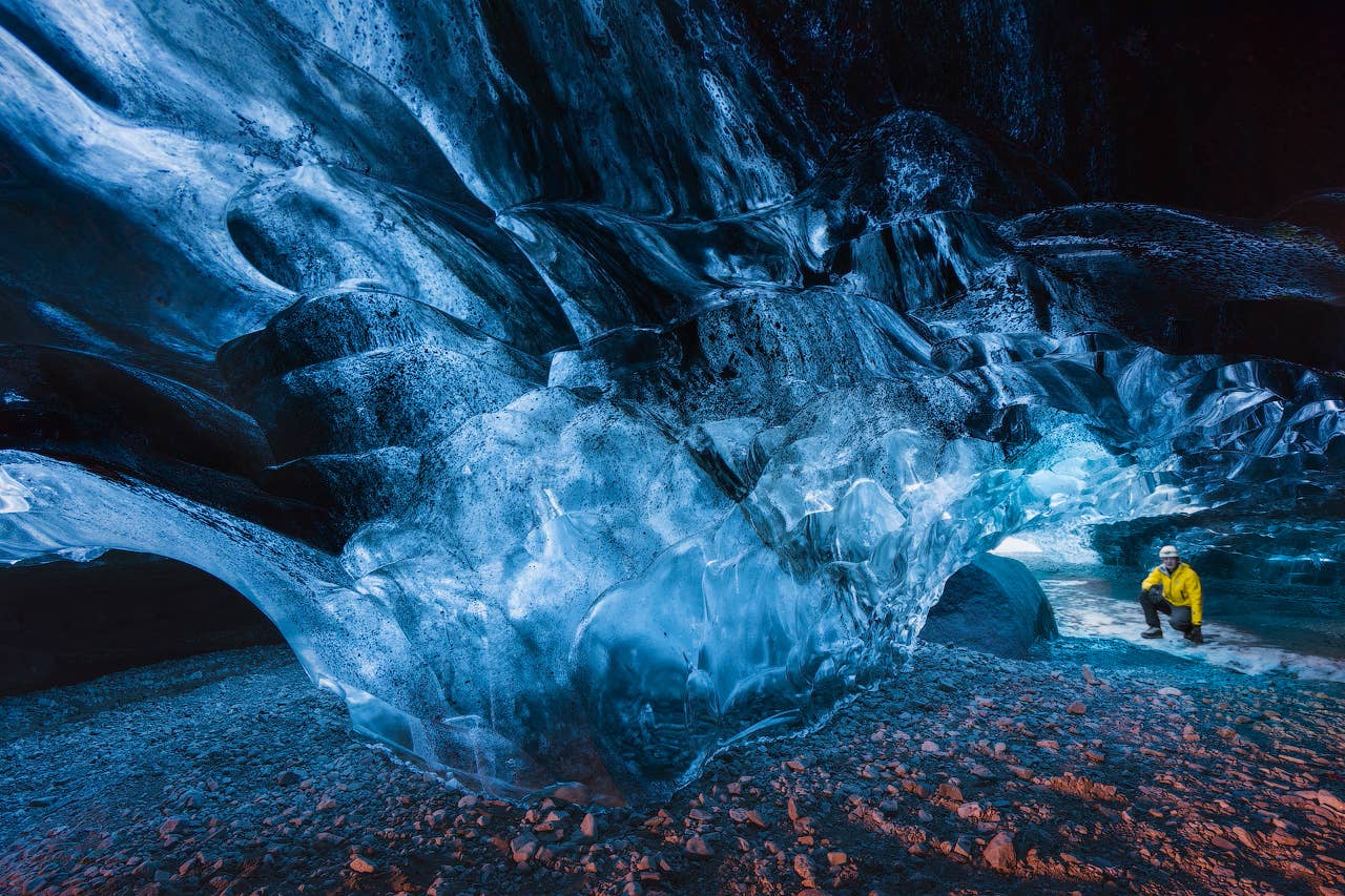 En rejsende iført en gul jakke udforsker en levende blå isgrotte i Vatnajökull Nationalpark på Island sydkyst.