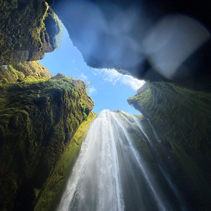 Gljufrabui Waterfall in Iceland viewed from inside the canyon, with sunlight streaming through moss-covered cliffs.