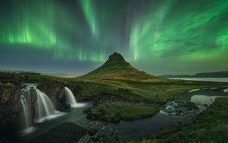 Det ikoniska konformade berget Kirkjufell och vattenfallet Kirkjufellsfoss är upplysta av livfulla gröna norrsken på västra Island.