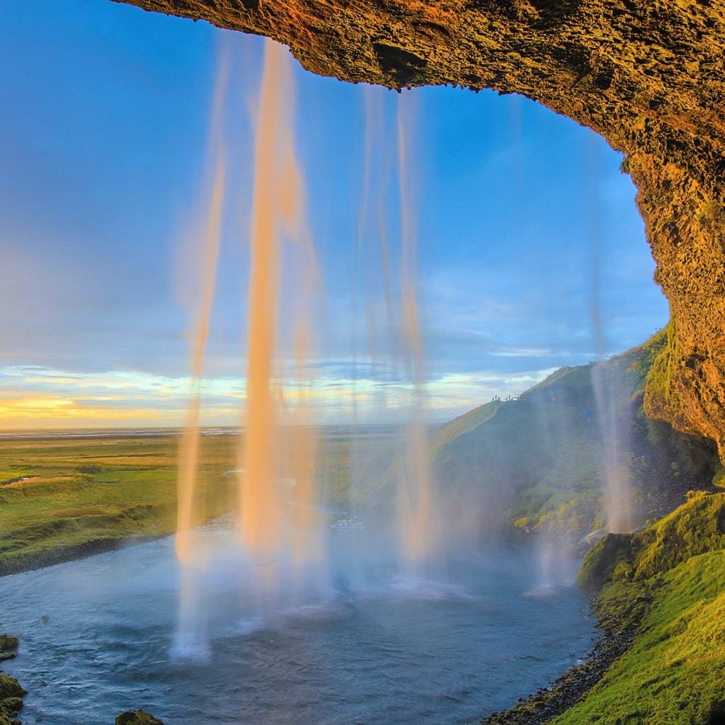 A view from behind the Seljalandsfoss waterfall overlooking the Icelandic landscape below.