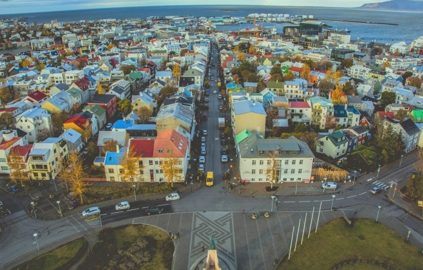 A view looking down on Reykjavik City with its colorful buildings and the coastline in the distance.