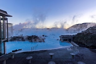 People bathing in the Blue Lagoon geothermal spa amid a natural landscape with steam rising into the air.