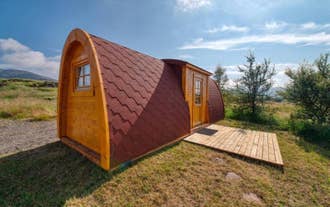 Exterior view of one of the Fossatun camping pods with a rounded roof, patio in front, and grass and trees around.