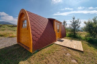 Exterior view of one of the Fossatun camping pods with a rounded roof, patio in front, and grass and trees around.