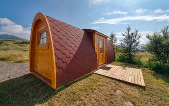 Exterior view of one of the Fossatun camping pods with a rounded roof, patio in front, and grass and trees around.