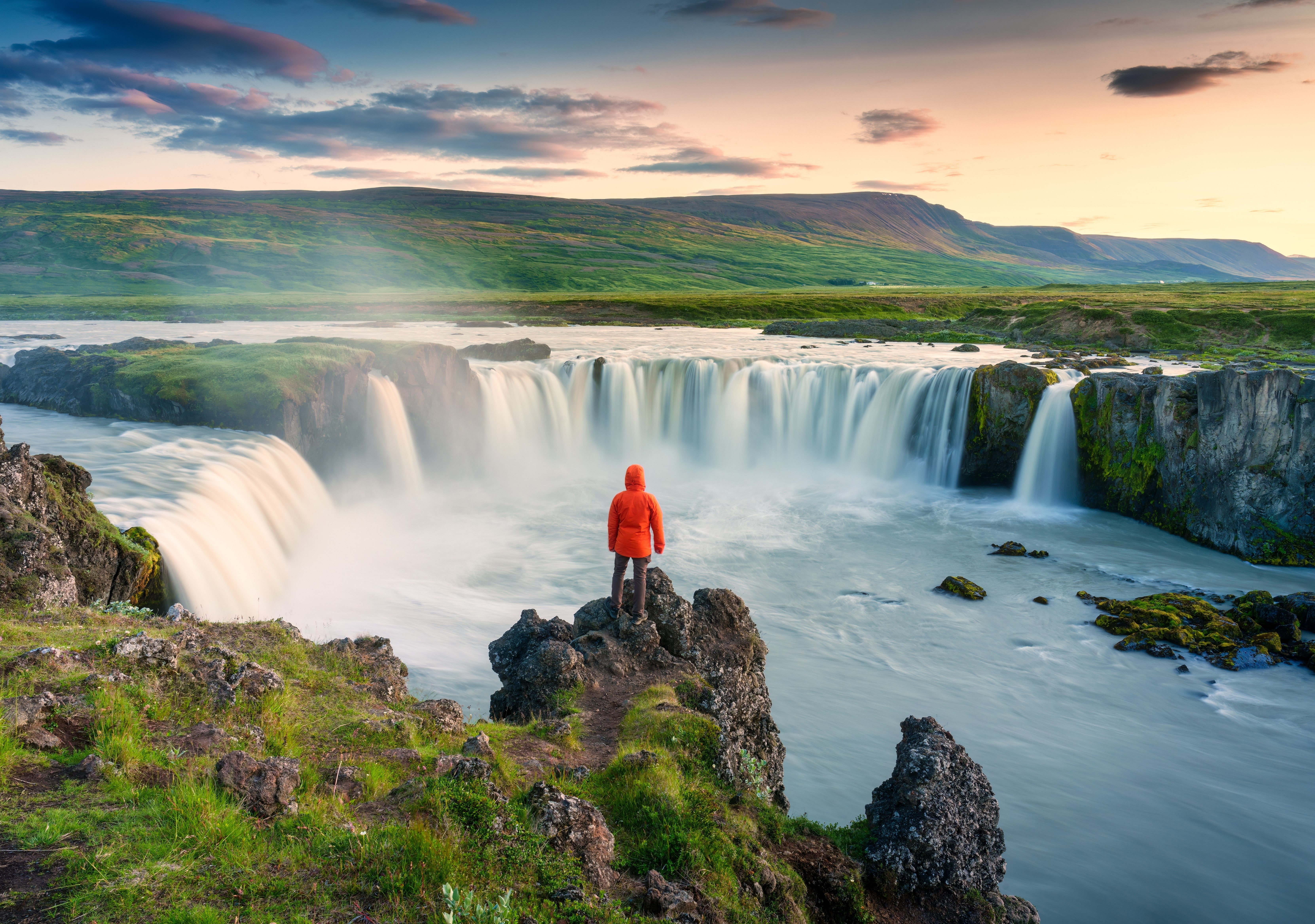 A person standing by the cliff of the Godafoss Waterfall in North Iceland.