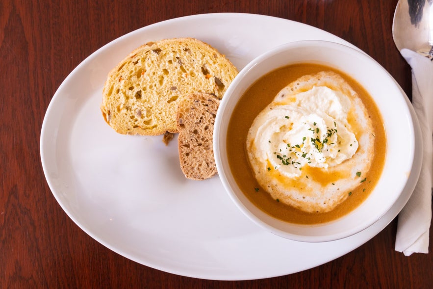 Bowl of creamy lobster soup served with fresh bread on a white plate.
