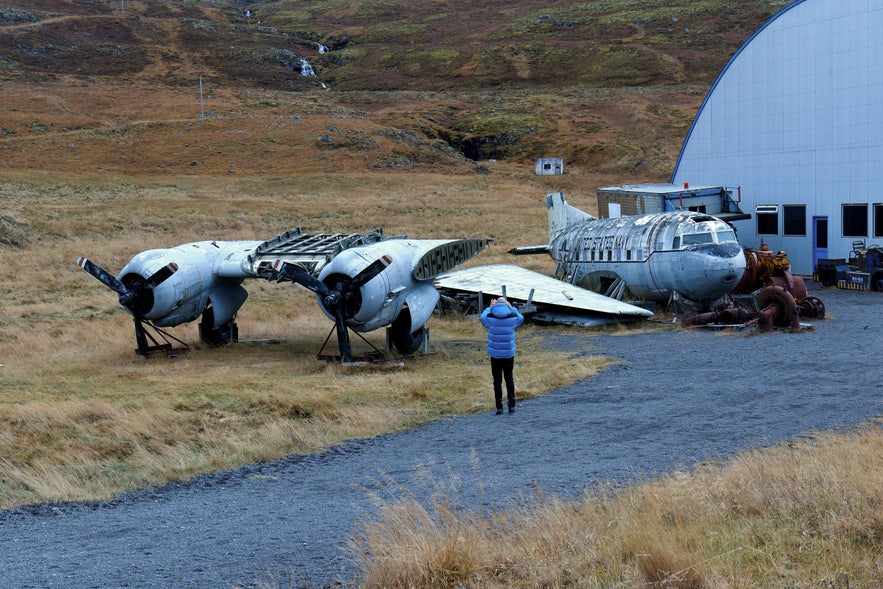 Visitor photographing retired military aircraft displayed outside Hnjotur Museum in Iceland.