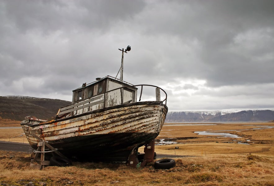 Abandoned wooden fishing boat overlooking a fjord near Hnjotur Museum in Iceland.