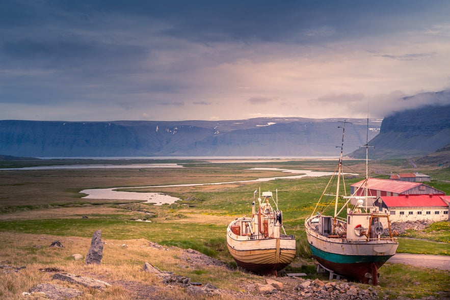 Old fishing boats and red-roofed buildings overlooking a fjord near Hnjotur Museum in Iceland.