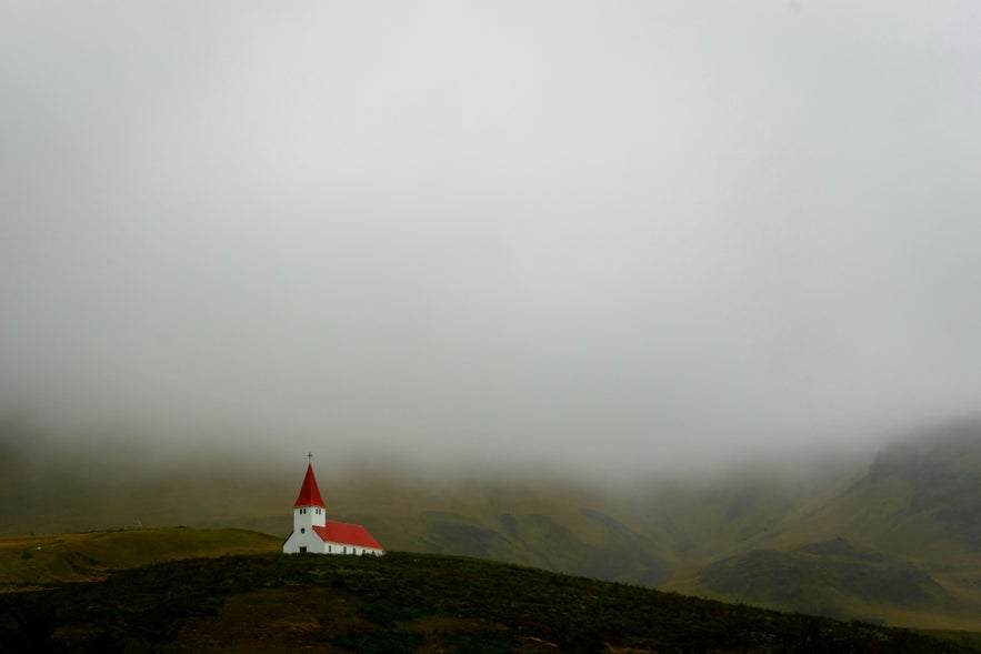 The red-roofed Vik i Myrdal Church, surrounded by fog, on top of the Vik Village in Iceland.