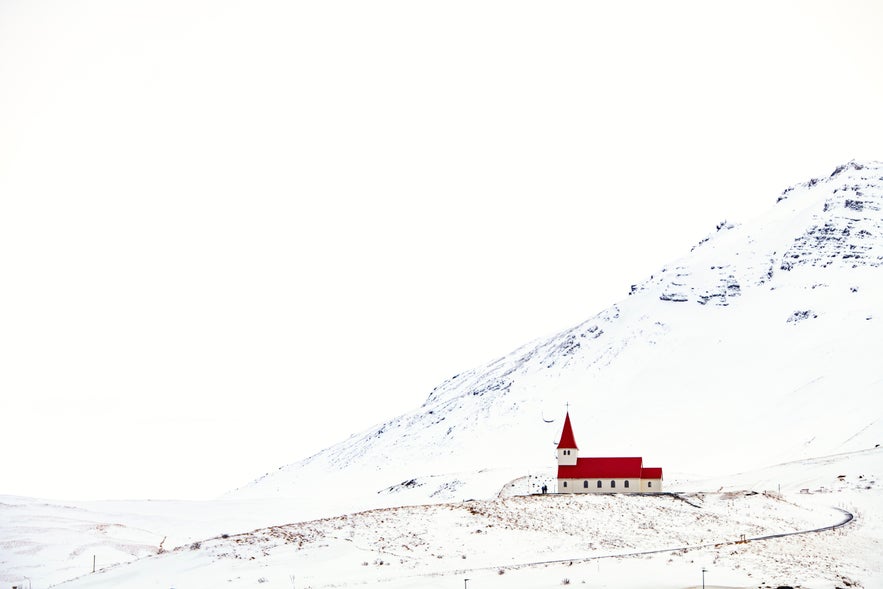 The red-roofed Vik i Myrdal Church on top of a snowy hill in Iceland.