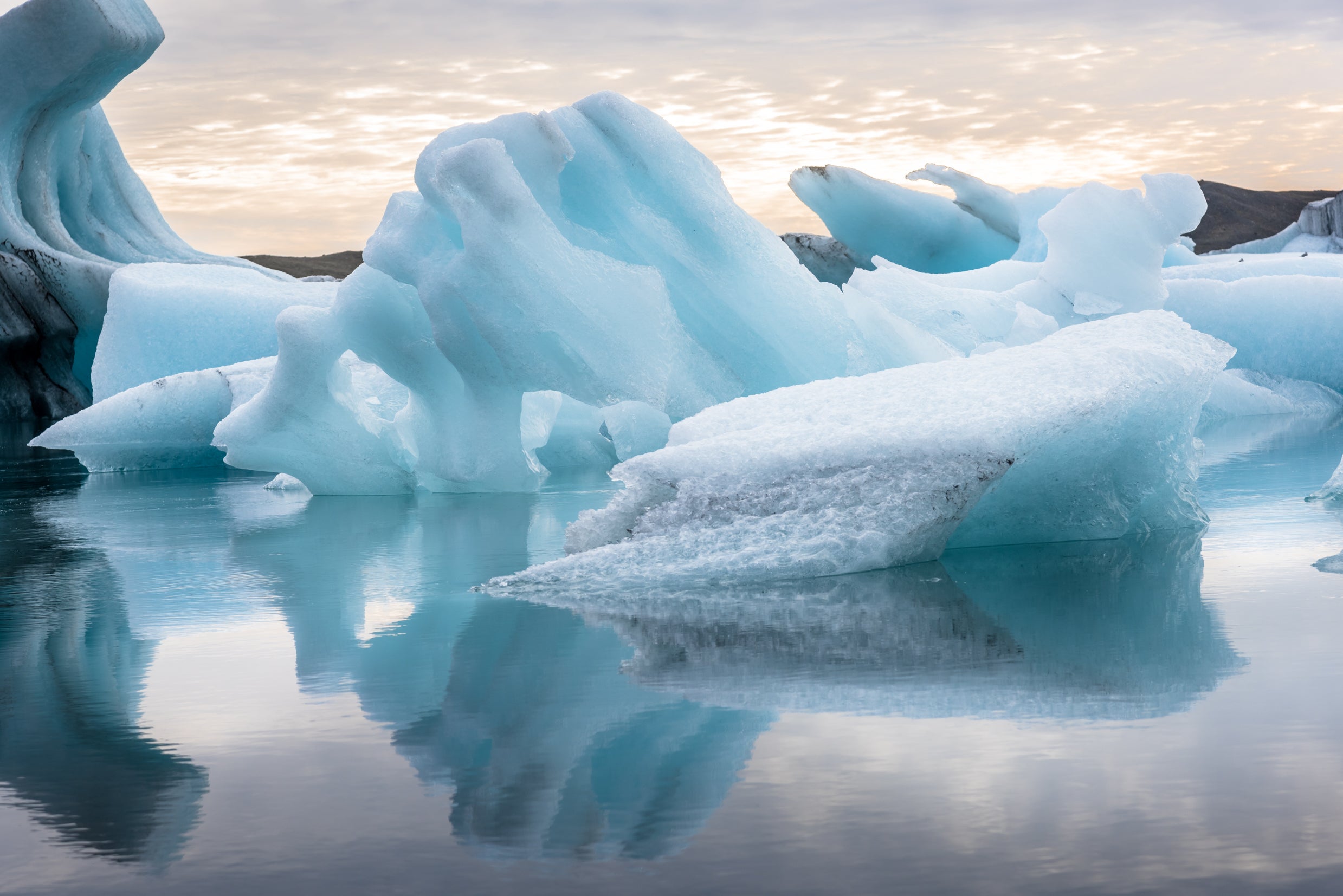 Krystalblå isbjerge flyder fredeligt i det gletsjervand i Jökulsarlon-gletsjerlagunen i Island ved solopgang.