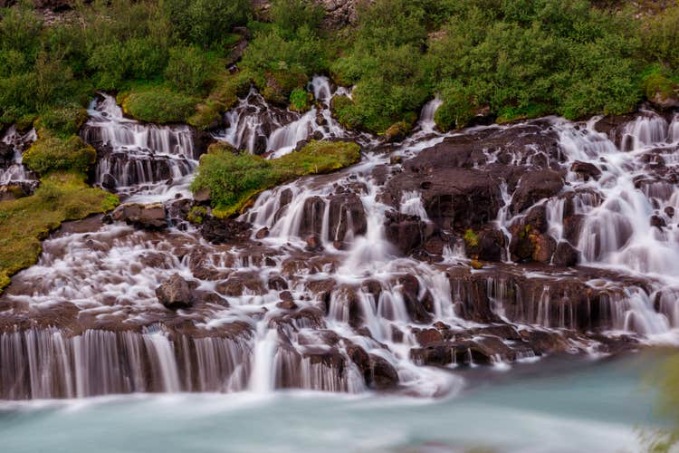 Small, gentle streams of Hraunfossar waterfalls emerging from dark volcanic rocks.
