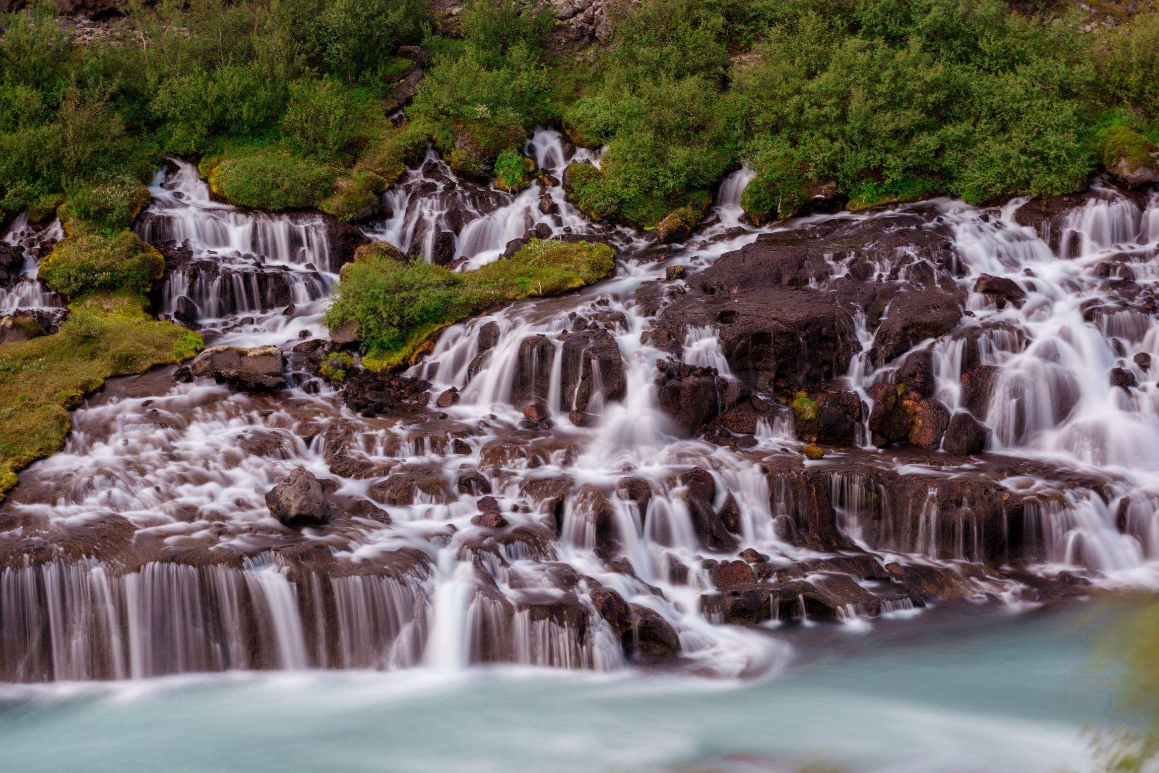 Small, gentle streams of Hraunfossar waterfalls emerging from dark volcanic rocks.
