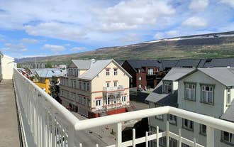 Balcony view overlooking neighboring rooftops and distant hills under a blue sky.