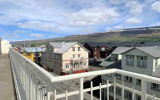 Balcony view overlooking neighboring rooftops and distant hills under a blue sky.