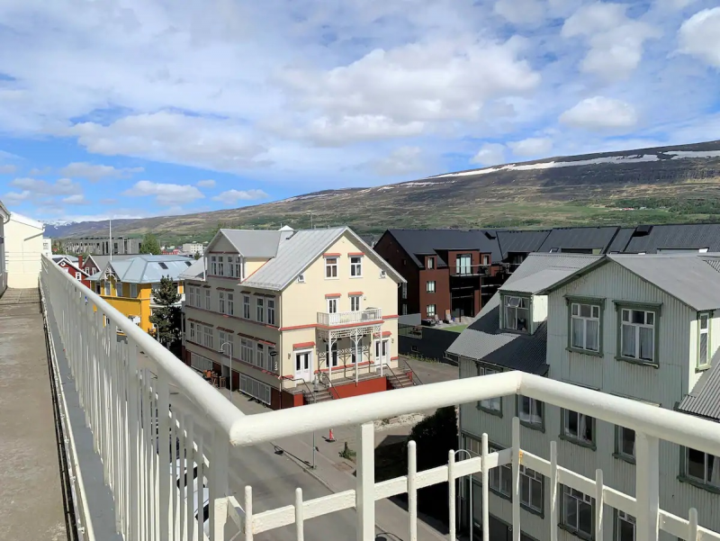 Balkonblick über Nachbardächer und entfernte Hügel unter blauem Himmel.