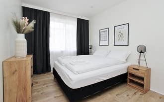 A bright bedroom at Downtown Apartments includes a double bed, blackout curtains, and minimalist framed art.