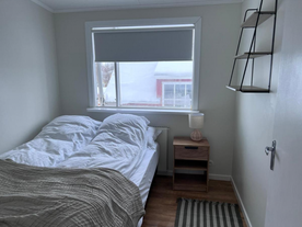 Cozy bedroom with a double bed, wooden nightstand, table lamp, and large window at M116 Historic Akureyri Apartments.