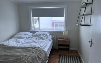 Cozy bedroom with a double bed, wooden nightstand, table lamp, and large window at M116 Historic Akureyri Apartments.