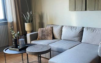 A modern living room with a large gray couch, round tables, plants, and a standing lamp.