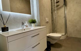 Modern bathroom featuring a white vanity, large mirror, toilet, and glass shower at Charming Deluxe Apartment in Akureyri.