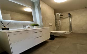 Modern bathroom featuring a white vanity, large mirror, toilet, and glass shower at Charming Deluxe Apartment in Akureyri.