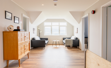 De bovenverdieping van het Big House With a View in Akureyri heeft comfortabele banken en een groot raam met uitzicht op de fjord.