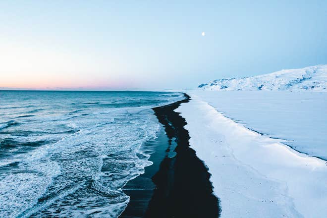 Winter waves crash along the snowy black sands of Reynisfjara Beach on the south coast of Iceland.