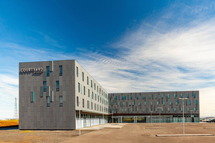 Exterior view of the Courtyard by Marriott Reykjavik Keflavik Airport on a bright and cloudy blue-sky day.