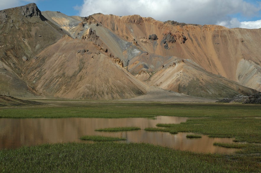 Montañas Sudurnámur en las tierras altas de Islandia, con laderas volcánicas en capas, colores terrosos y un humedal cubierto de hierba en primer plano Montañas Sudurnámur en las tierras altas de Islandia, con laderas volcánicas en capas, colores terrosos y un humedal cubierto de hierba en primer plano