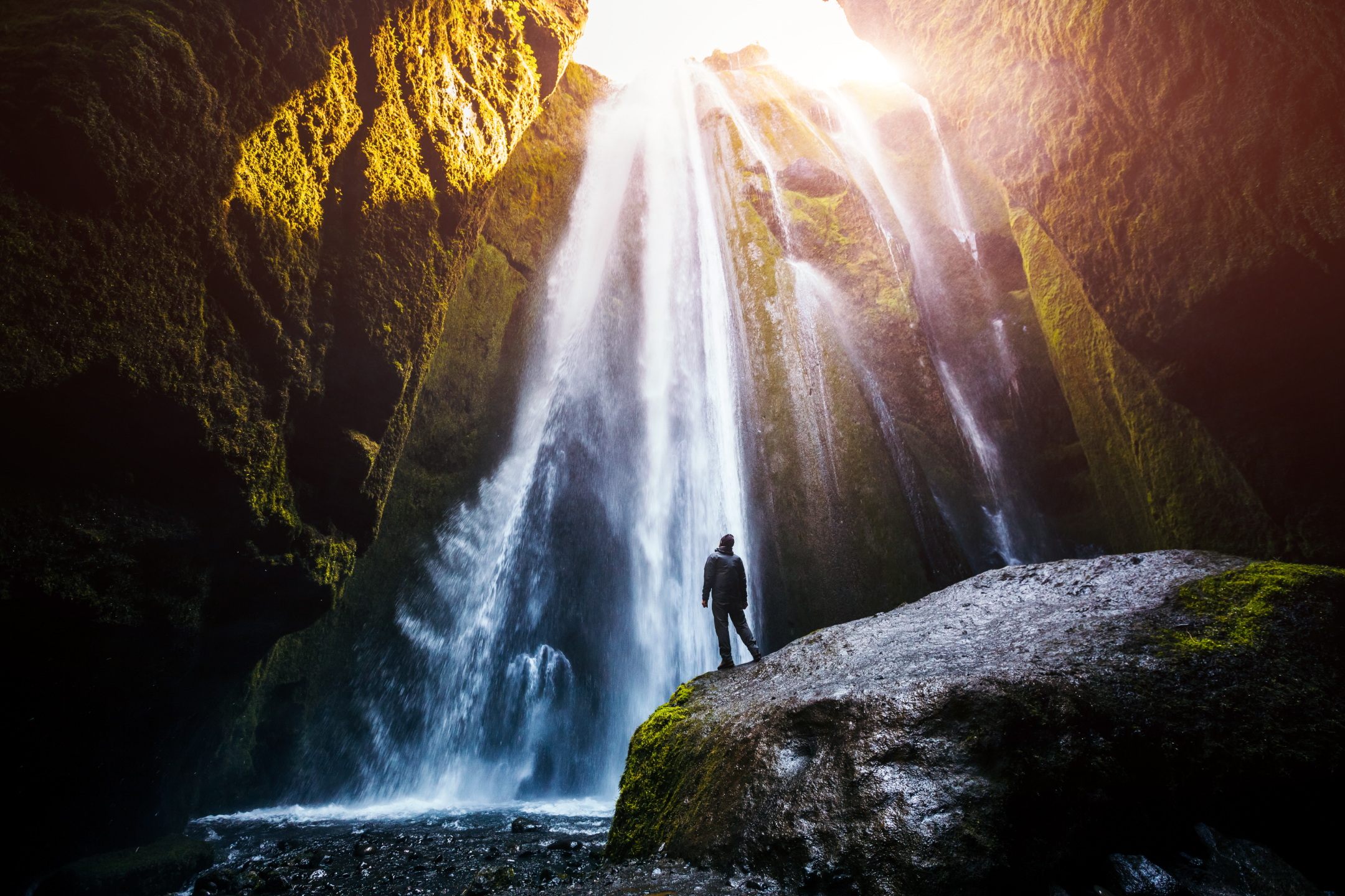 Traveler stands before Gljufrabjui Waterfall in South Iceland, gazing up at the hidden cascade streaming through moss-covered canyon walls.