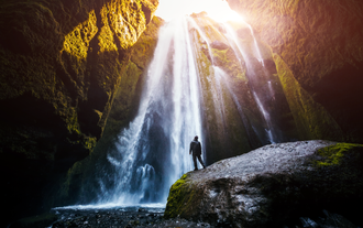 Traveler stands before Gljufrabjui Waterfall in South Iceland, gazing up at the hidden cascade streaming through moss-covered canyon walls.