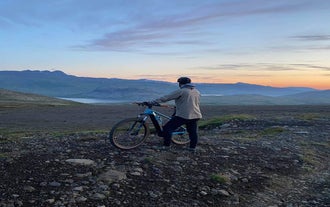 Ein Mann hält ein Mountainbike und blickt auf die Seen und Berge der Halbinsel Snaefellsnes.
