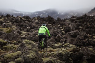 Hombre con abrigo impermeable, sobre rocas en una bicicleta de montaña.