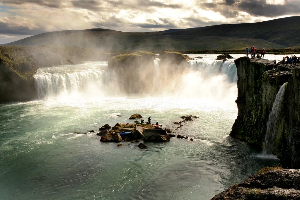 Tourists view Godafoss Waterfall in North Iceland with mist rising from the cascade.