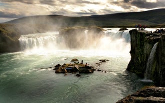 Tourists view Godafoss Waterfall in North Iceland with mist rising from the cascade.