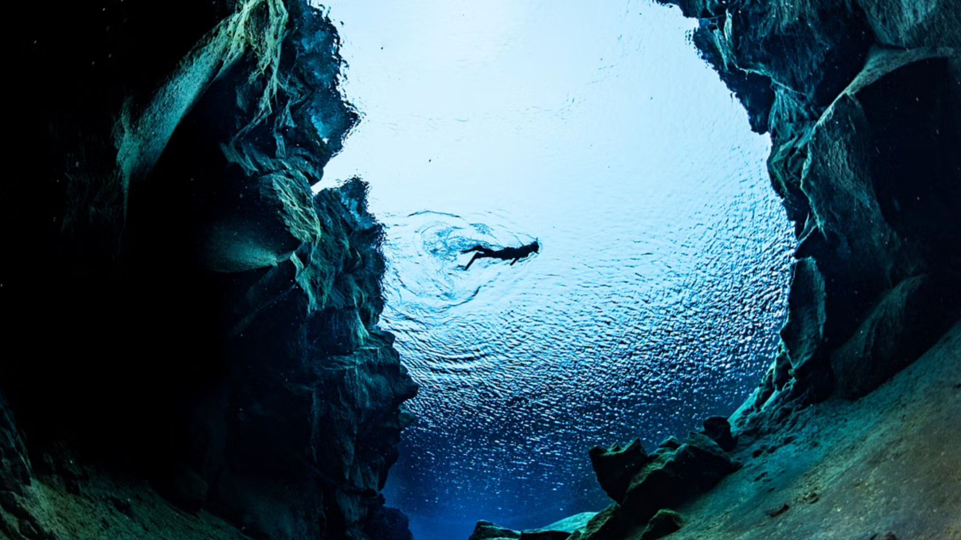 A diver swims in between continental rifts on a Silfra snorkeling tour.
