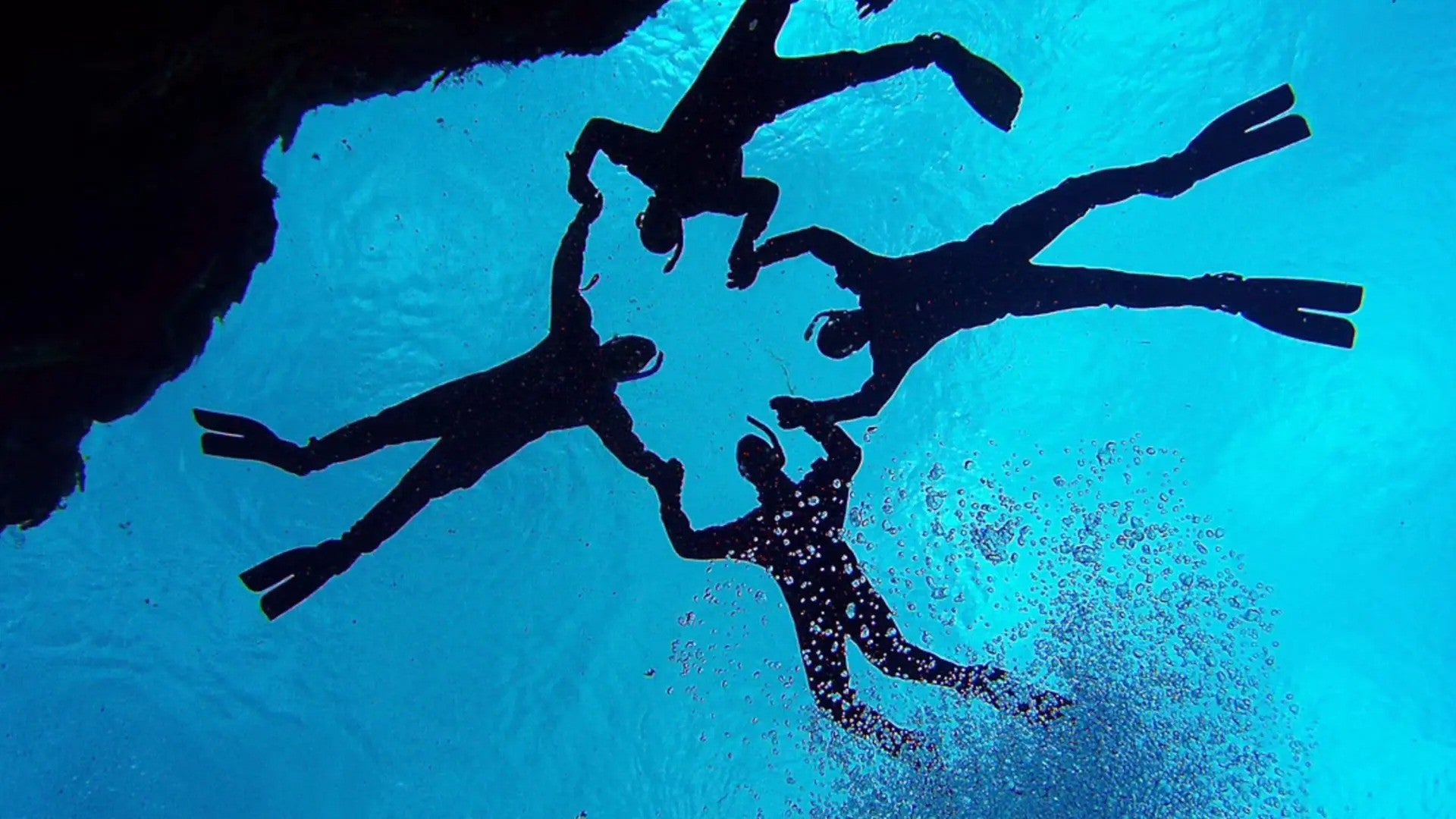 The silhouette of four divers make a deep contrast against the blue waters of Silfra Fissure on a snorkleling tour